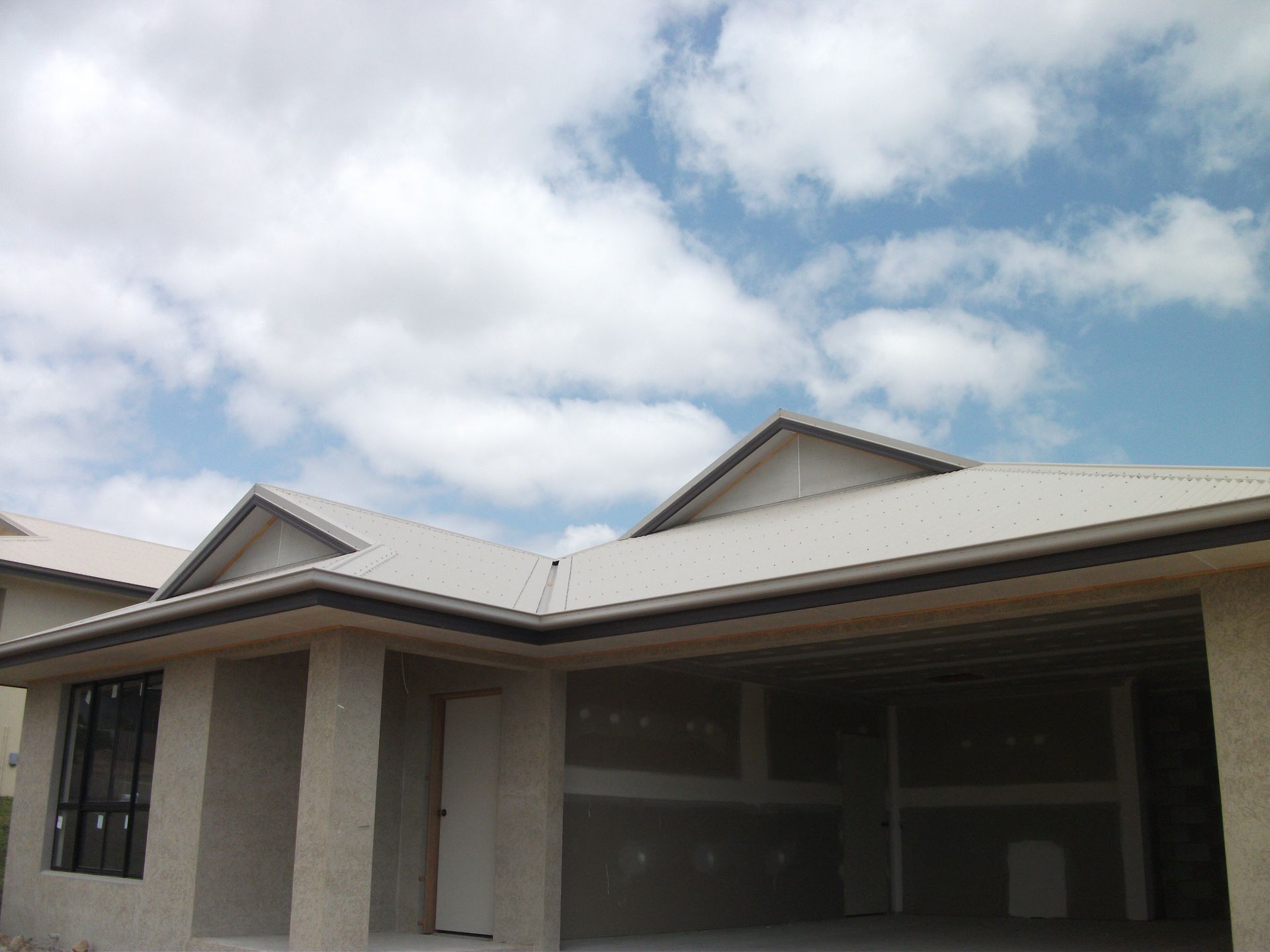 A Trucks Parked in Front of a New House With Unfinished Roof Under a Cloudy Sky — Roof 4 U in Alice River, QLD
