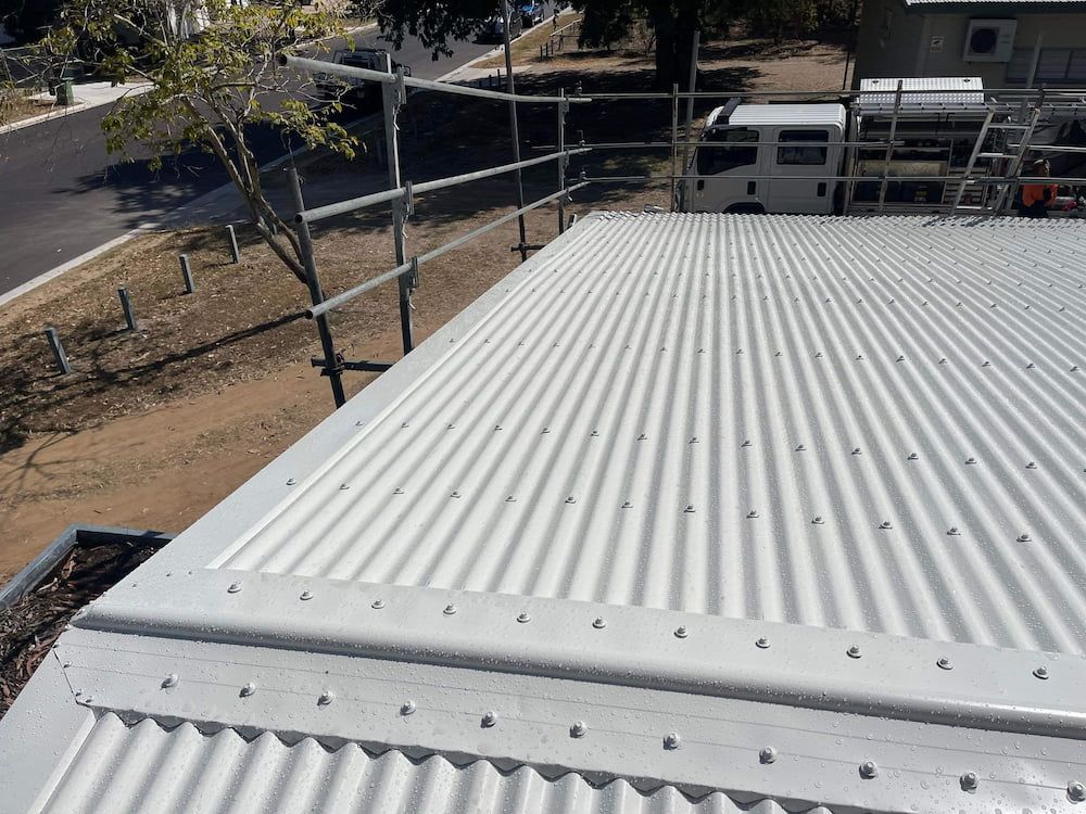 White Corrugated Metal Roof With Safety Railing and Background of Trees and a Road — Roof 4 U in Alice River, QLD