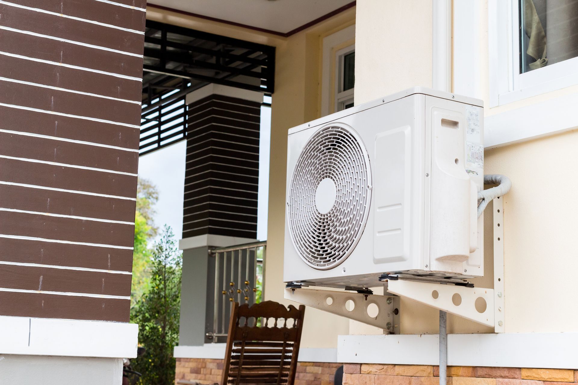 White air conditioner unit mounted on a beige house wall. Brown wooden siding is visible to the left.