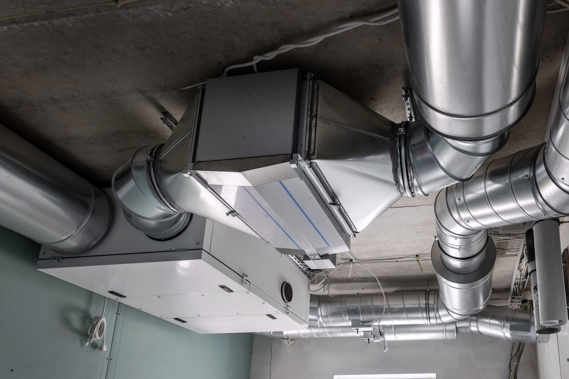Ventilation system ductwork installed on a concrete ceiling in a building under construction.