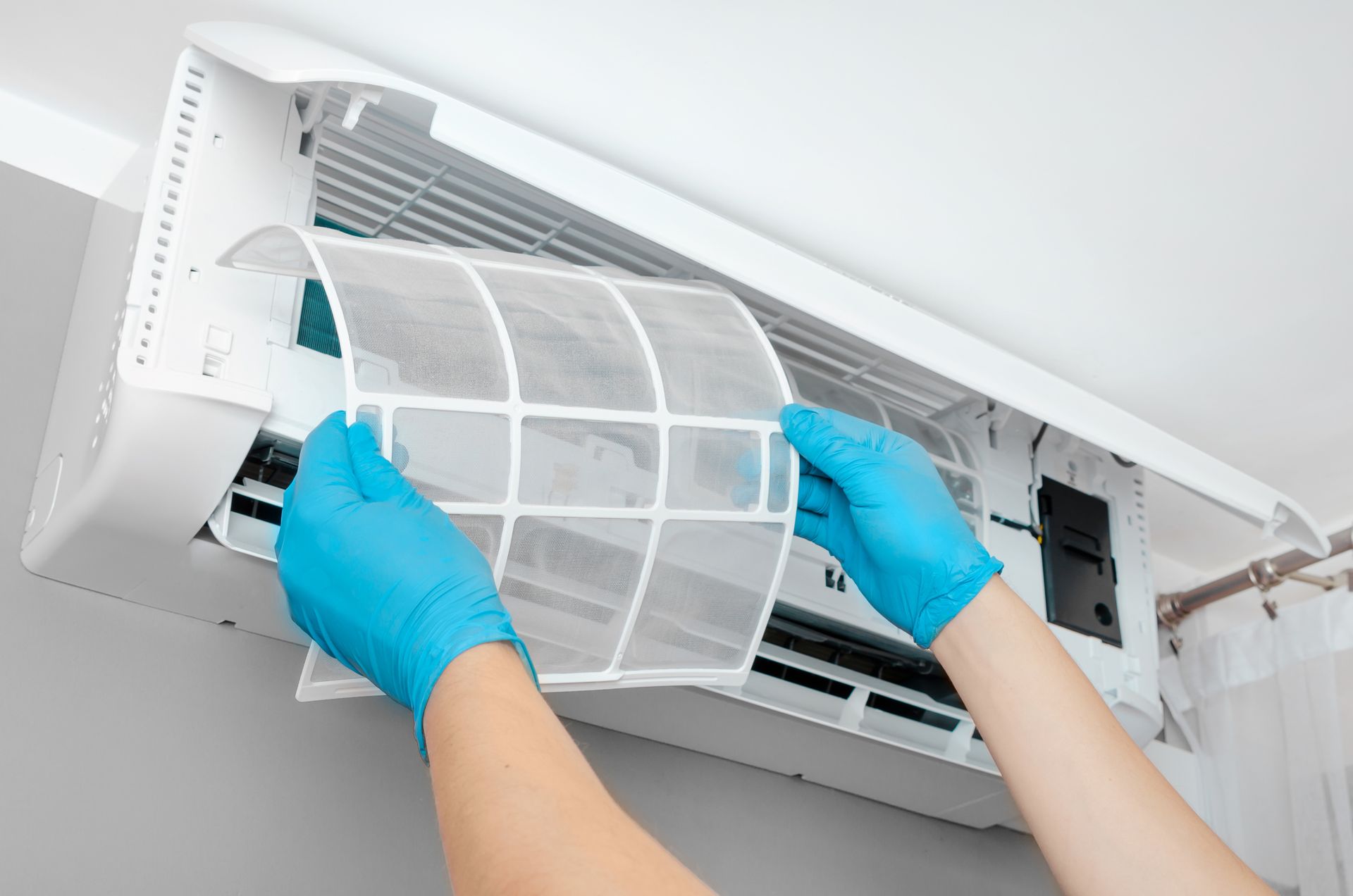 Person in blue gloves removing an air conditioner filter.