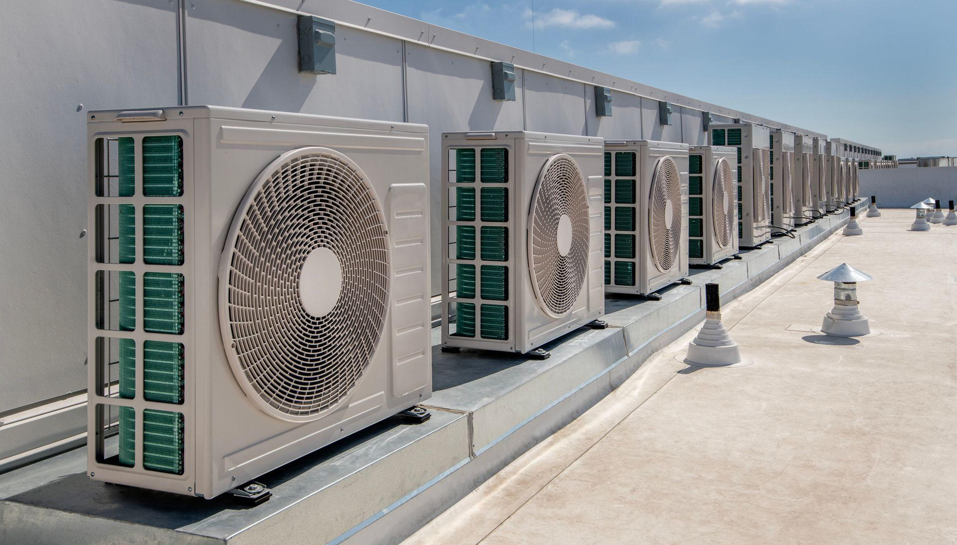 Row of white air conditioning units on a rooftop under a blue sky.