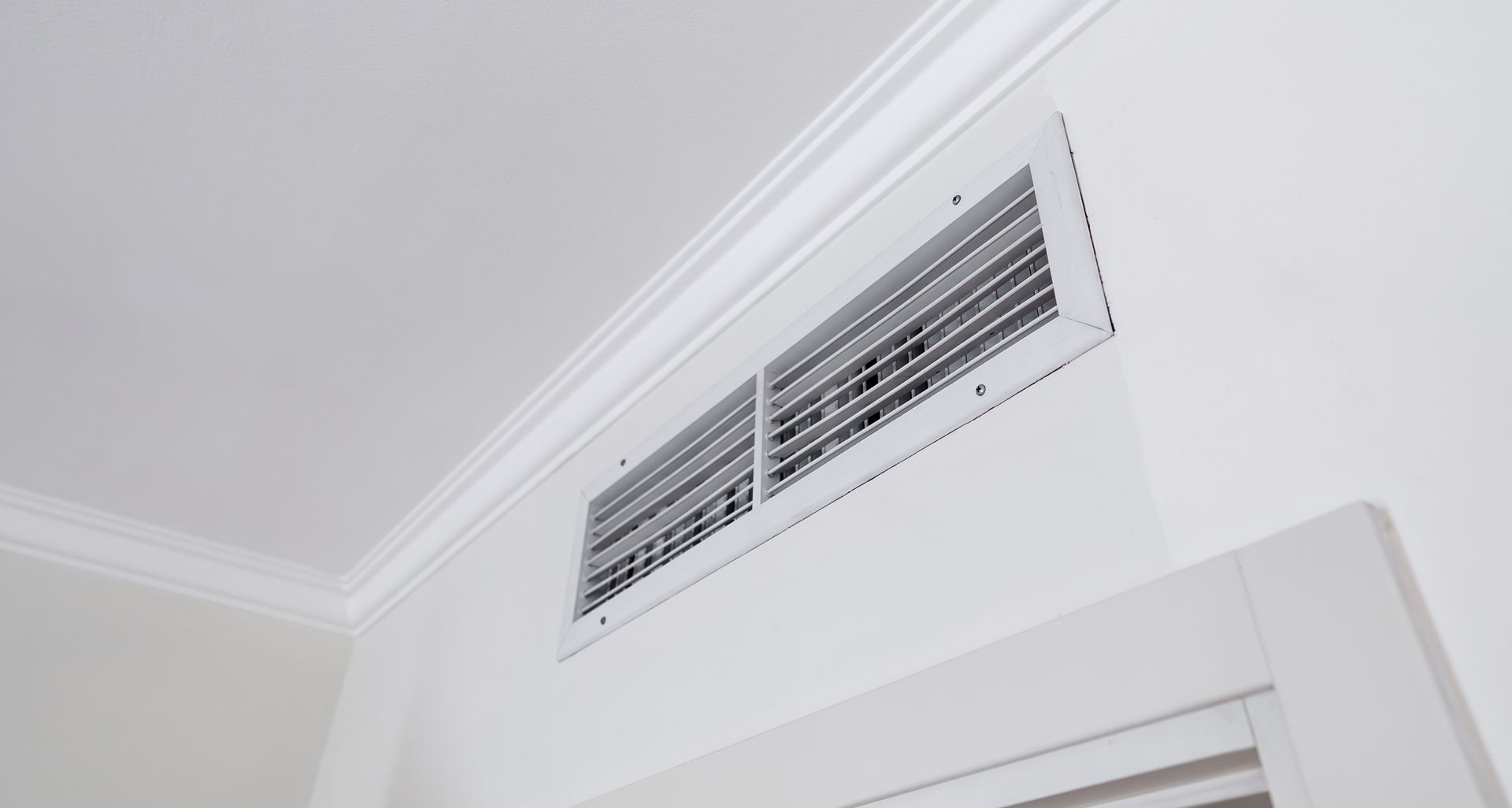 White air vent in a white wall near a white ceiling with crown molding.