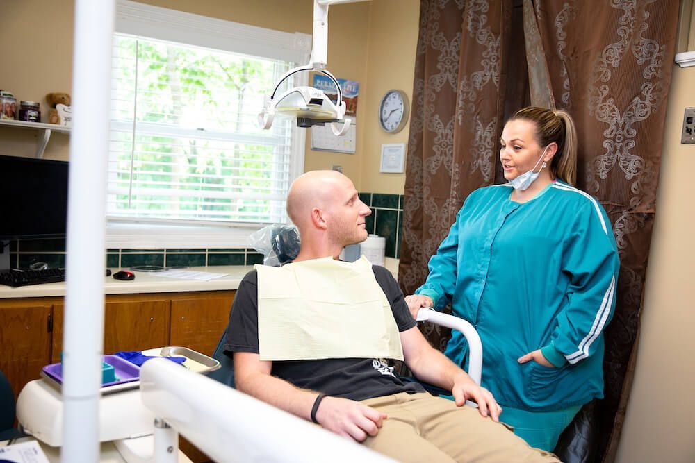 A woman is standing next to a man in a dental chair.
