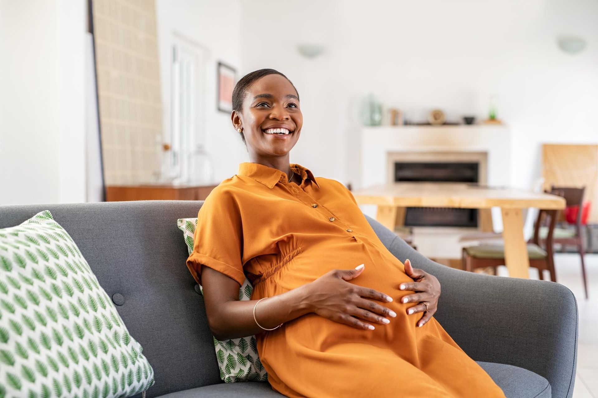 A pregnant woman is sitting on a couch holding her belly.