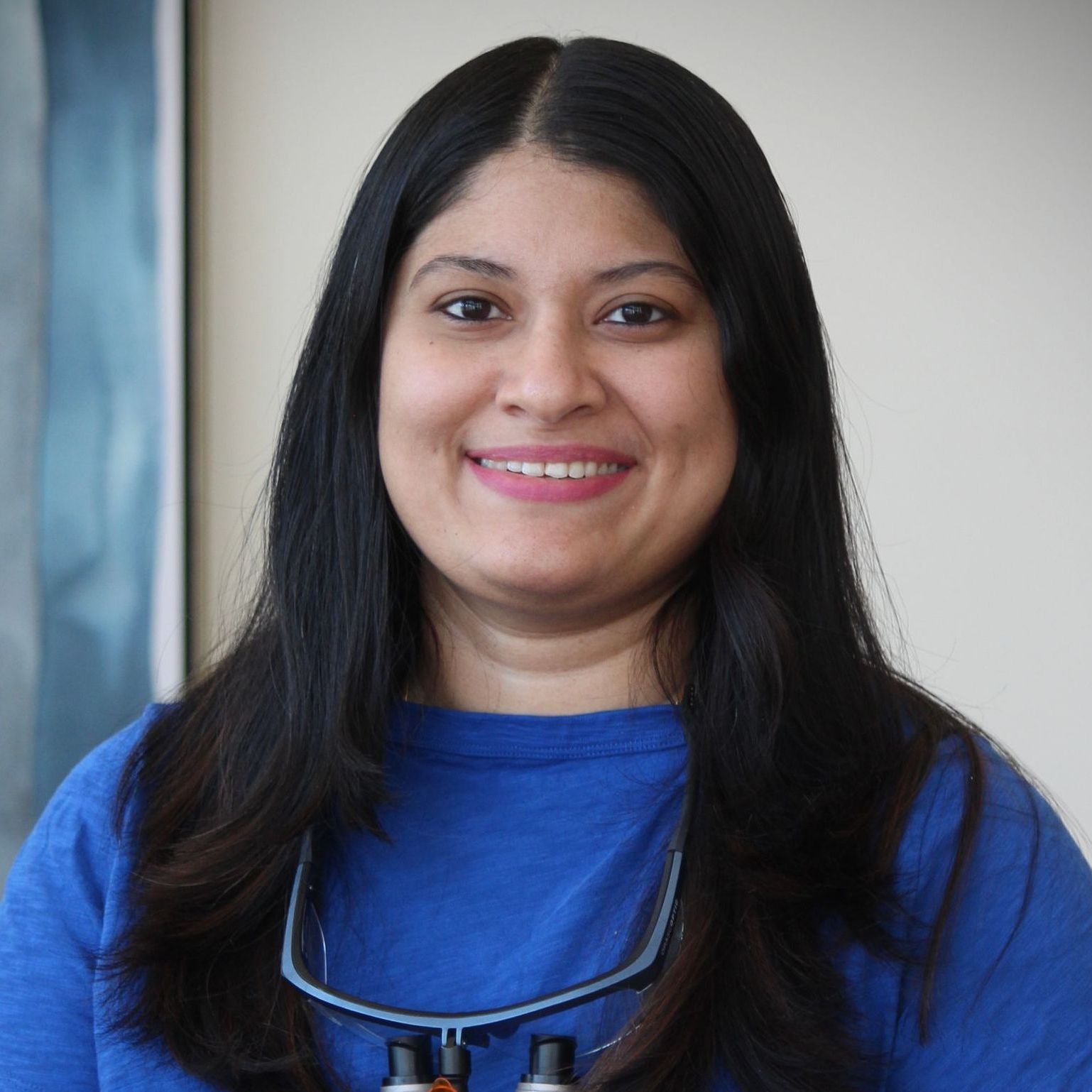 A woman wearing a blue shirt and a necklace is smiling for the camera.