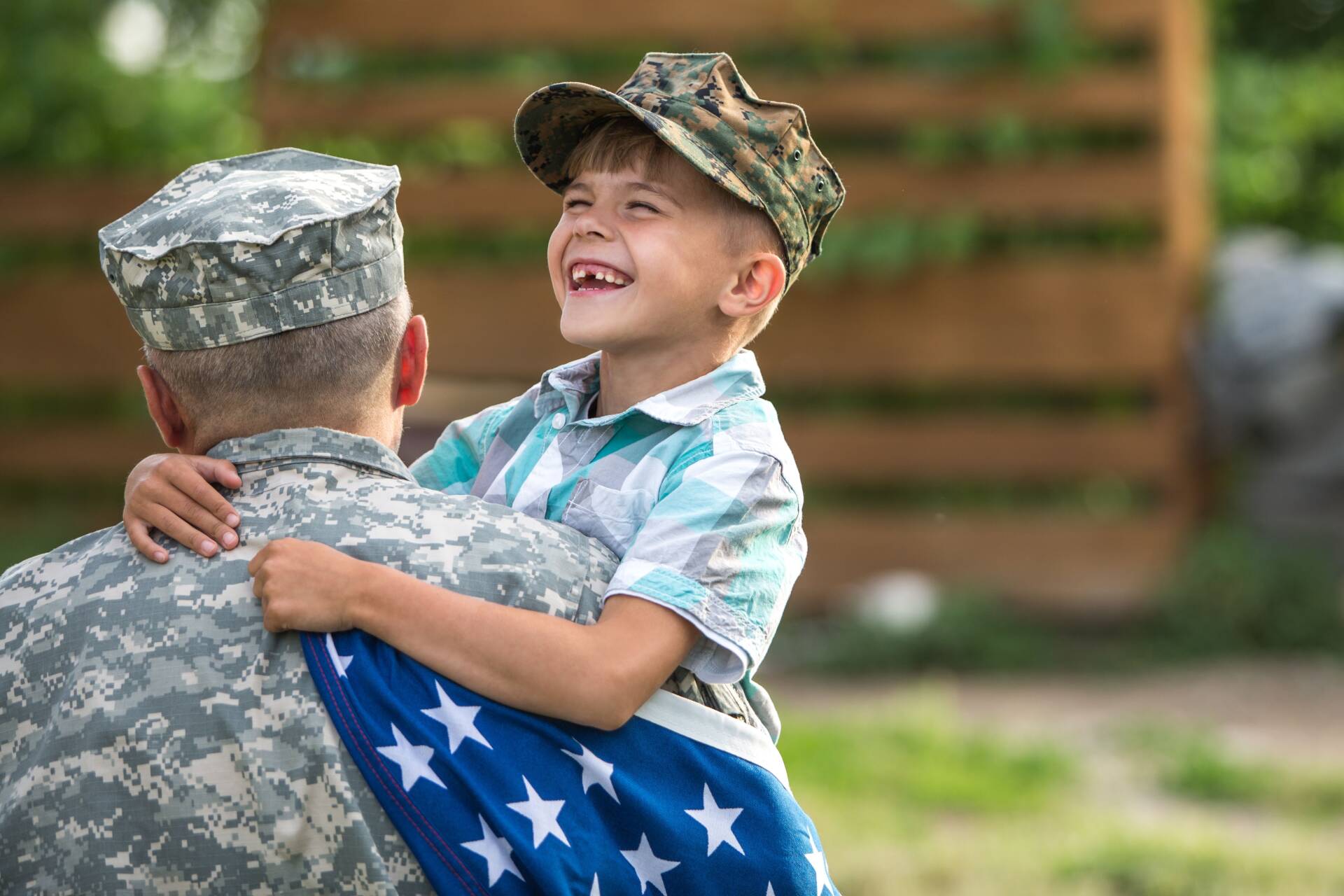 Son hugging military dad in uniform while carrying American flag
