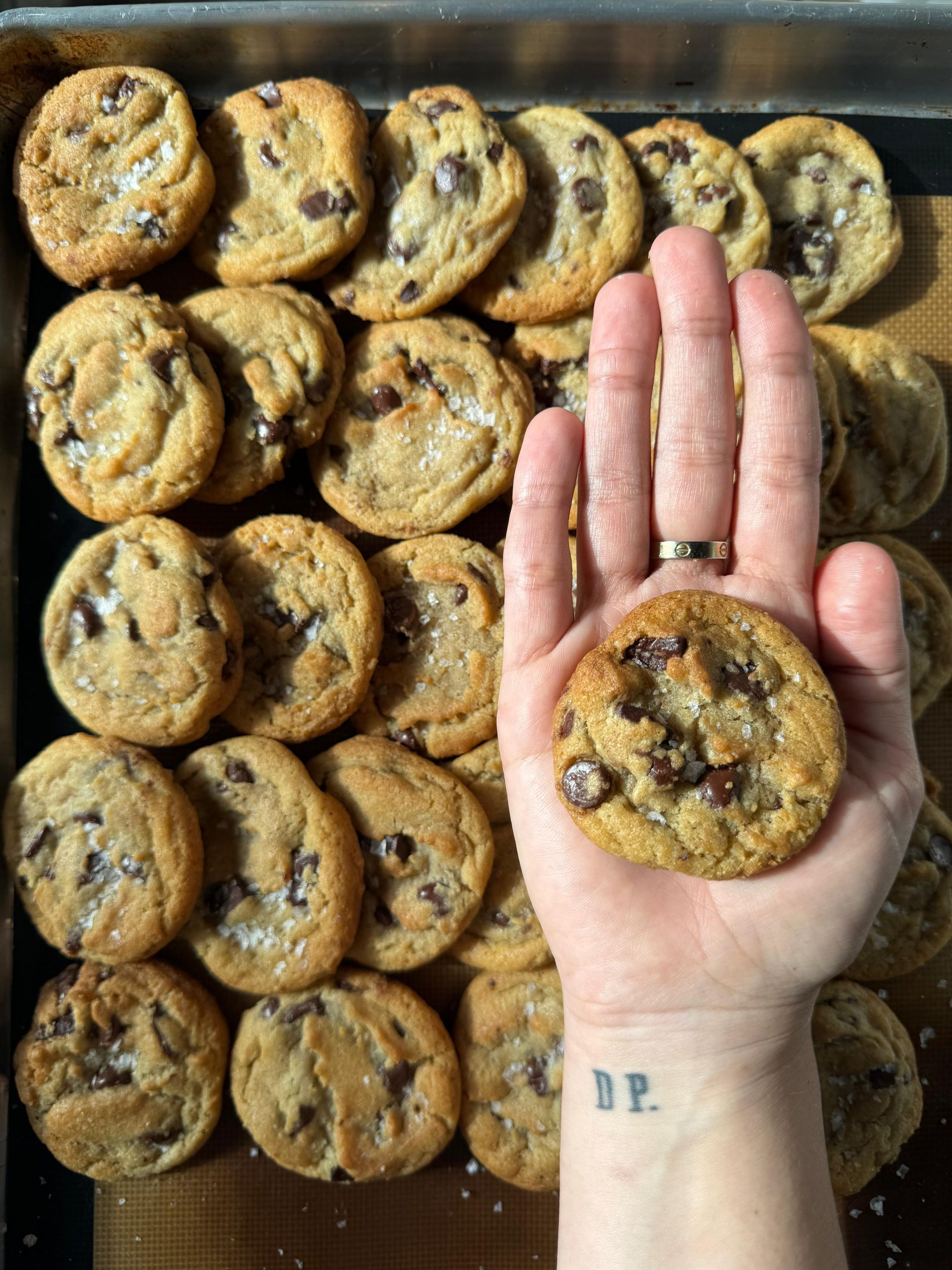 michele cruz the owner of dona posada is holding a freshly baked chocolate chip cookie in their hand.