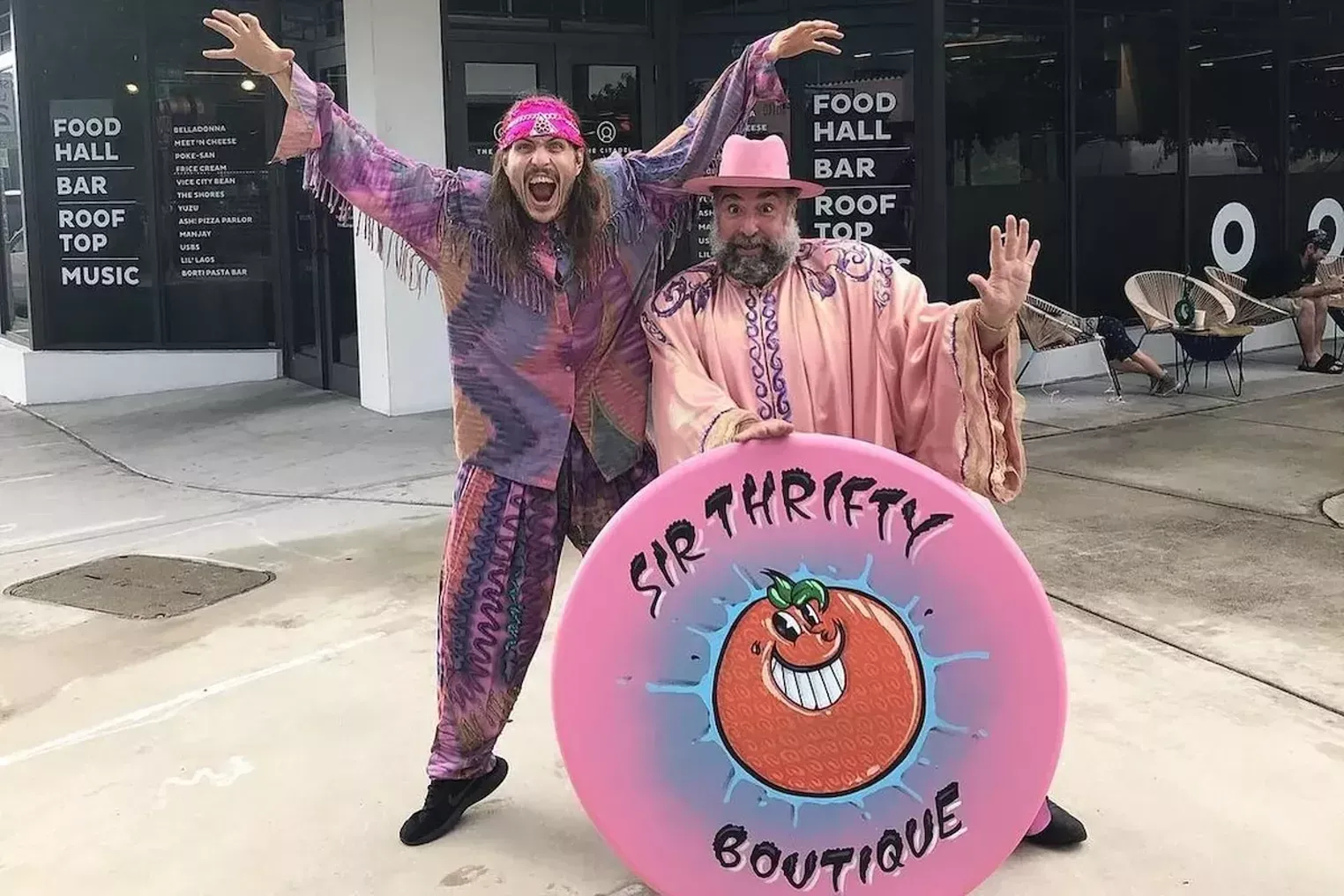 A man and a woman are standing next to a pink sign that says sir thrifty boutique.