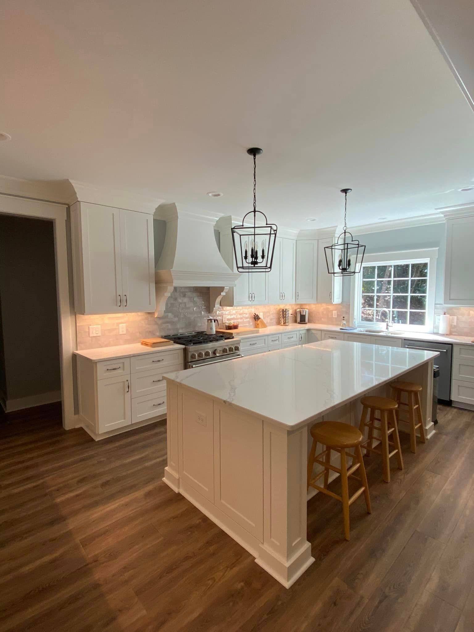 a kitchen with white cabinets , stools , a large island and a stove .