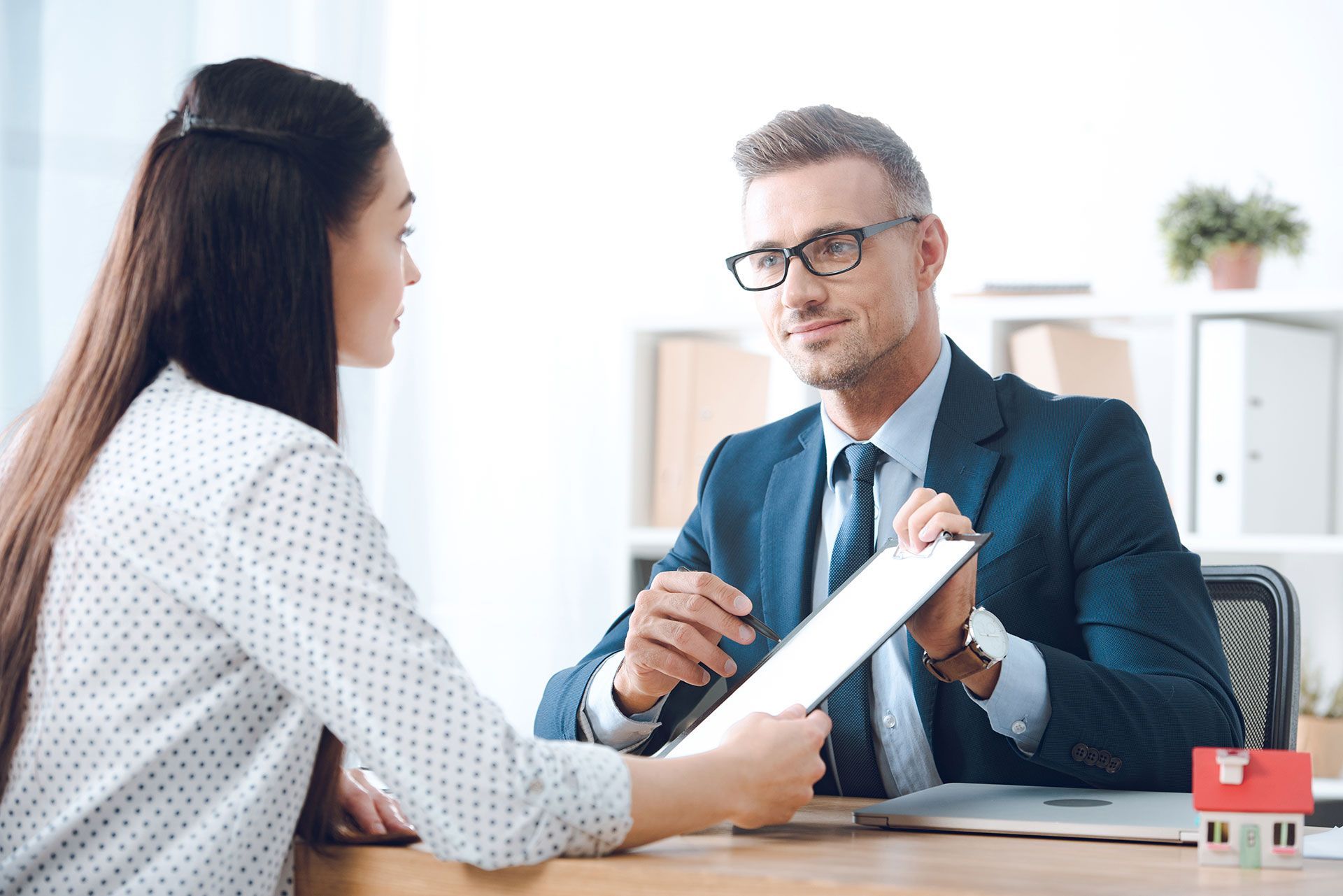 insurance agent pointing at clipboard in clients hand at tabletop in office, house insurance concept