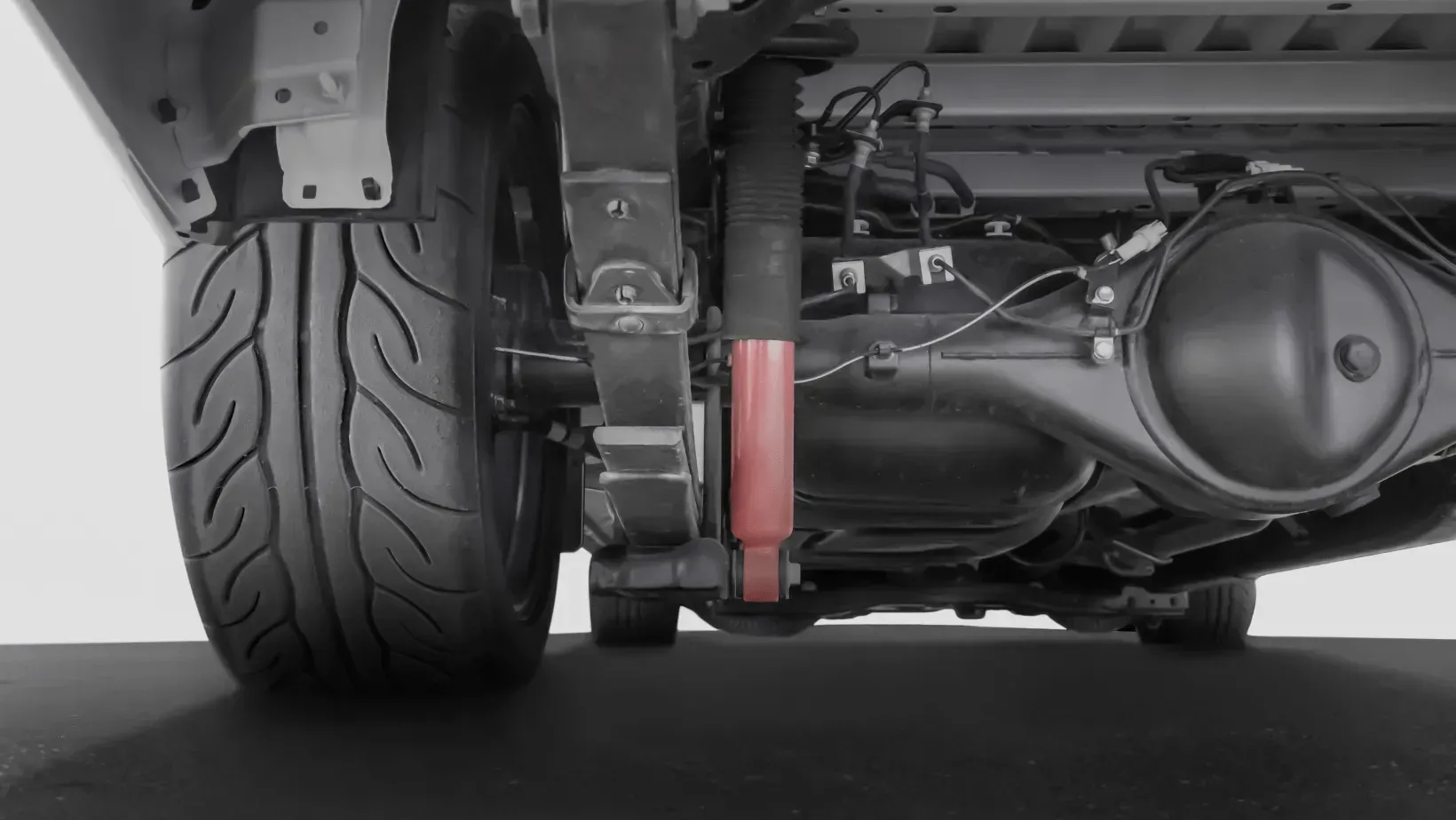 A mechanic in a red shirt and dark overalls works on the brake system of a car raised on a hydraulic lift in a garage.