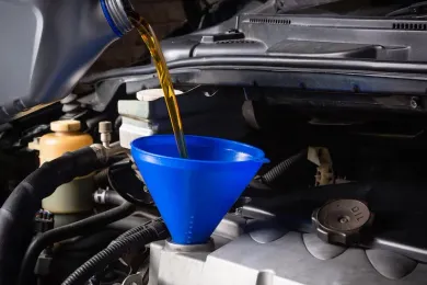 Golden motor oil being poured from a container through a blue plastic funnel into a car engine.