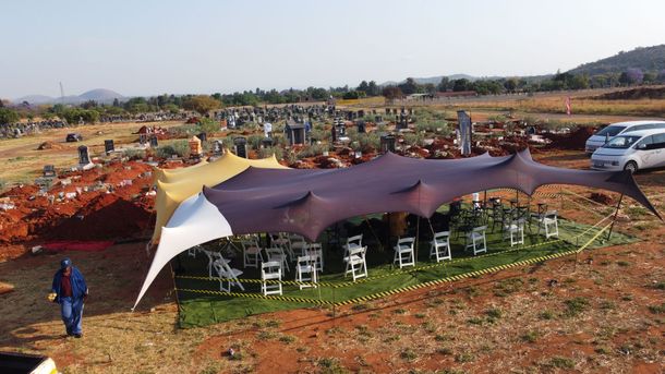 Stretch tent erected at a graveyard with chairs and a person walking nearby.