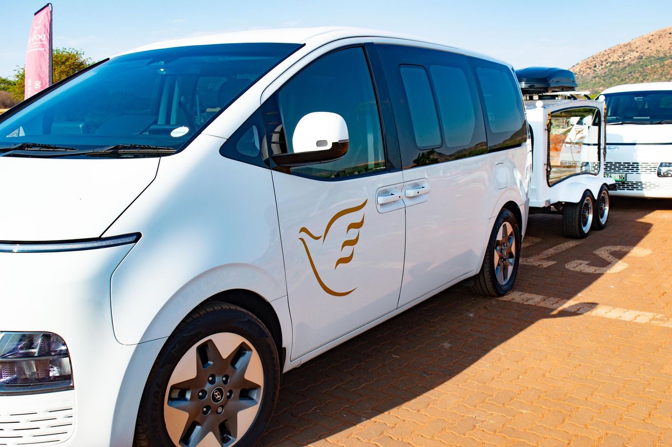 White minivan with gold logo and trailer, parked outdoors on a sunny day.