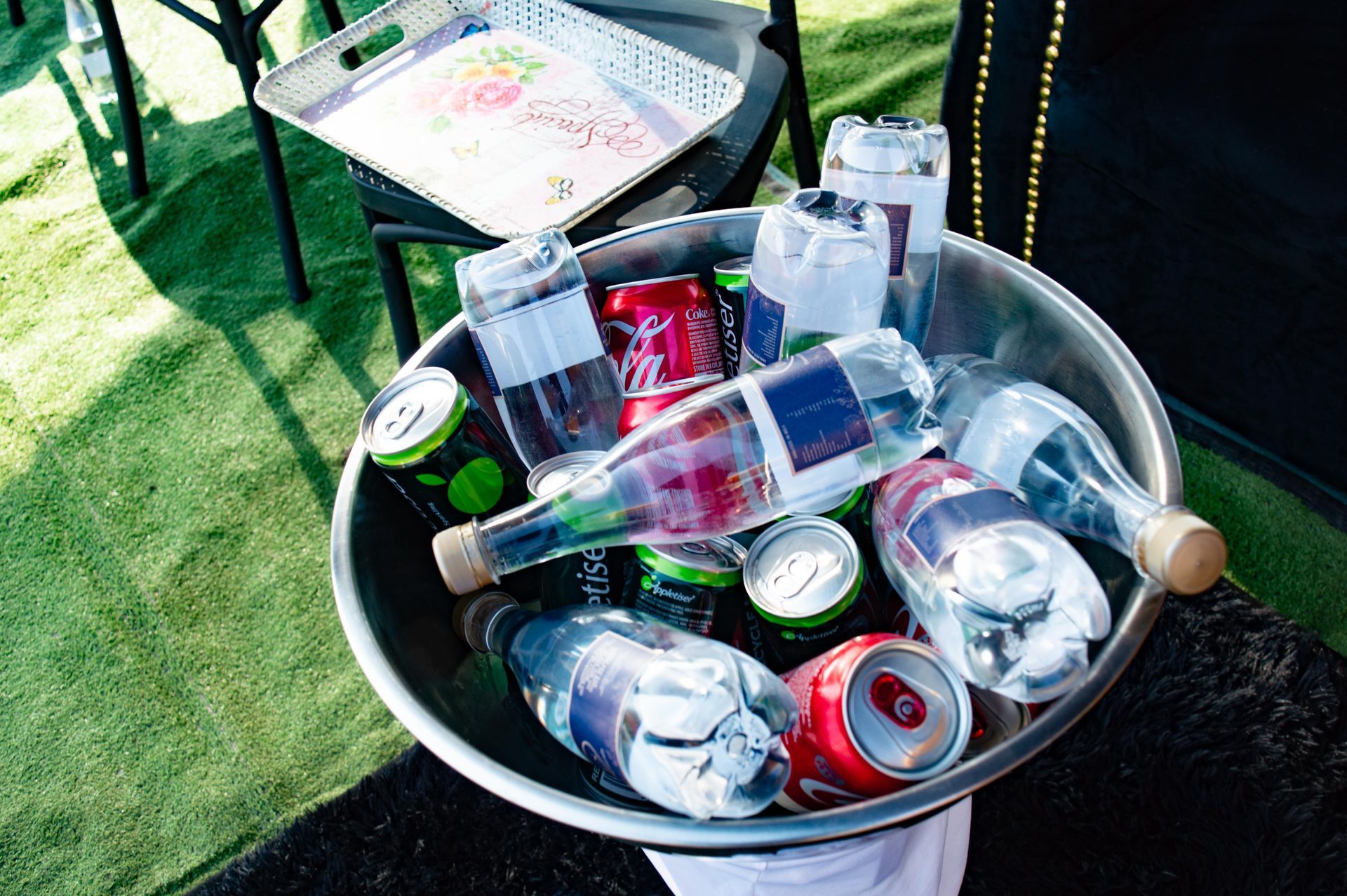 Metal bowl filled with empty soda cans and water bottles on green grass.