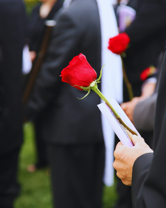 Person holding a red rose and a paper at a memorial service.