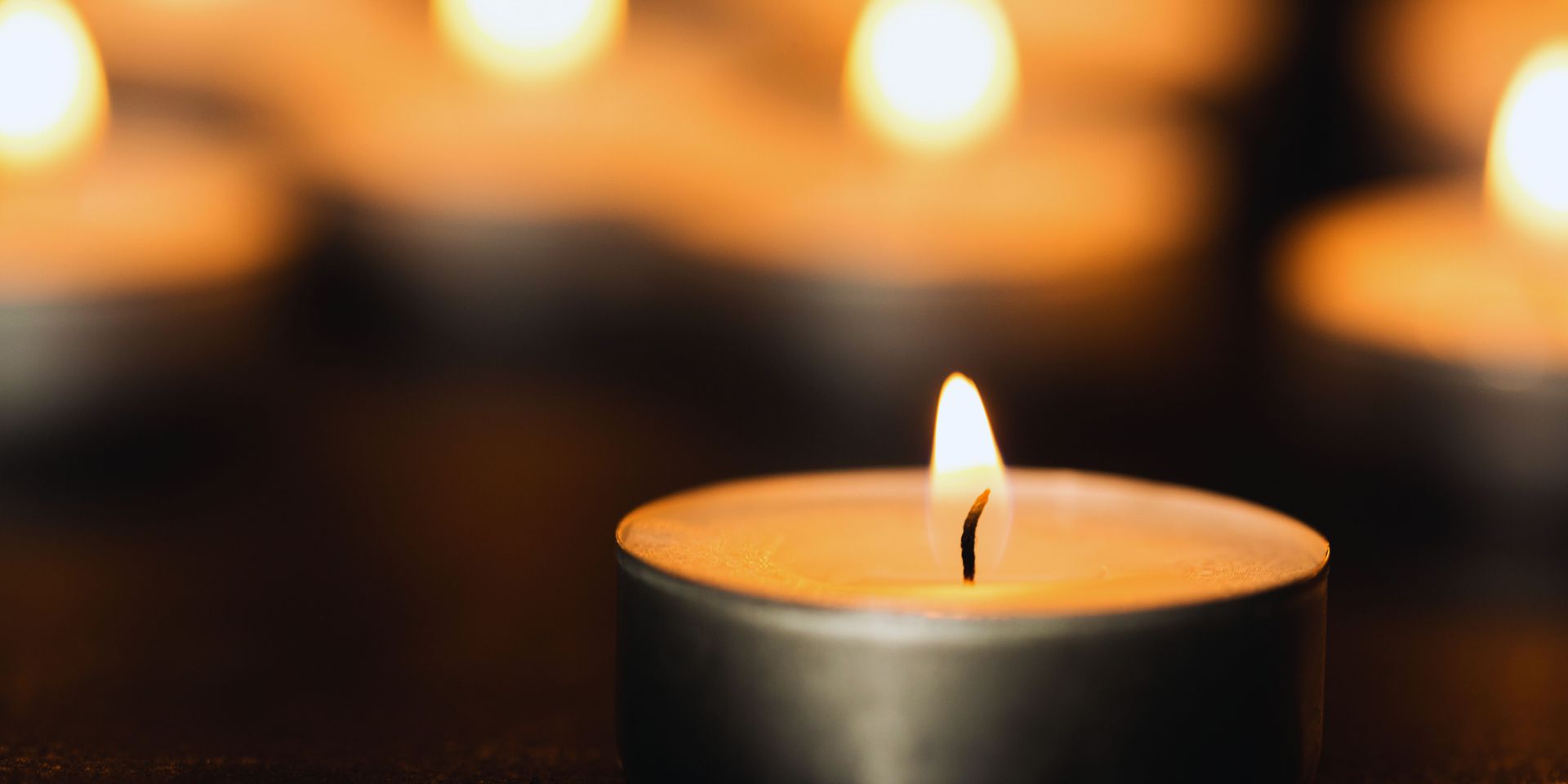 A lit tea light candle in focus, with other lit candles blurred in the background, creating a warm ambiance.