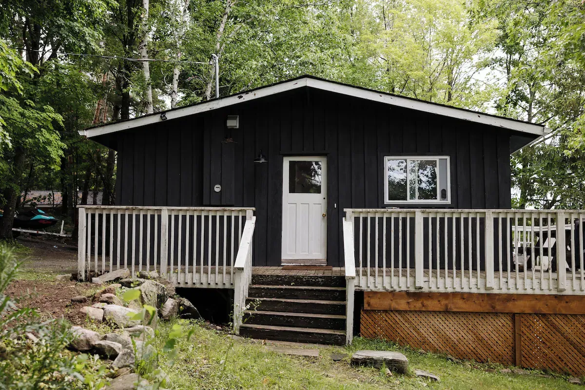 A small black house with a white deck in the woods.