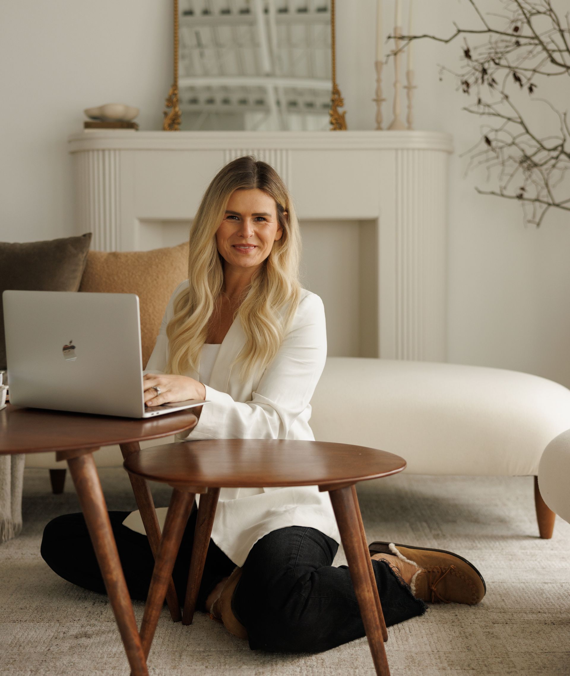 A woman is sitting on a white couch in a living room looking at her phone.