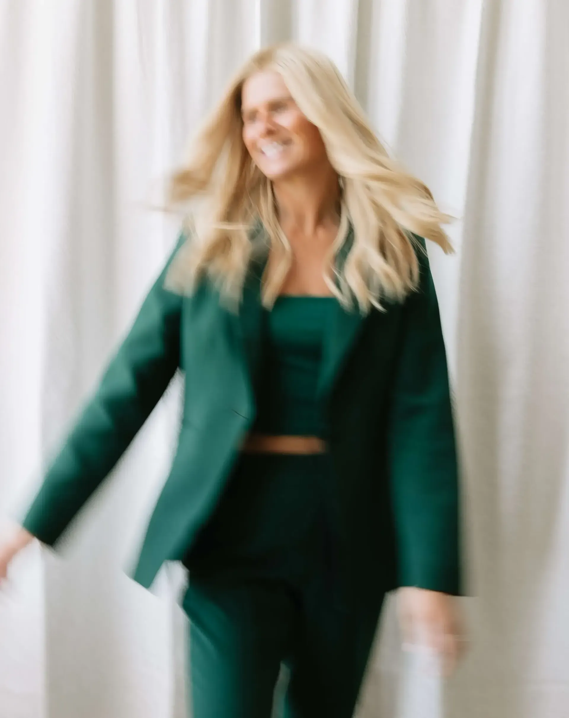 A woman in a green suit is standing in front of a white curtain.