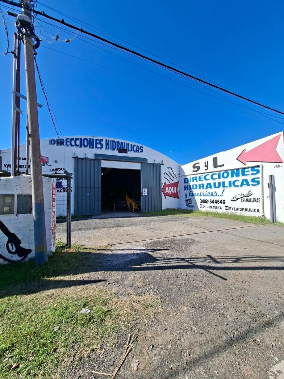 Edificio industrial blanco con letreros de SYL soluciones hidráulicas, visto desde un camino de grava