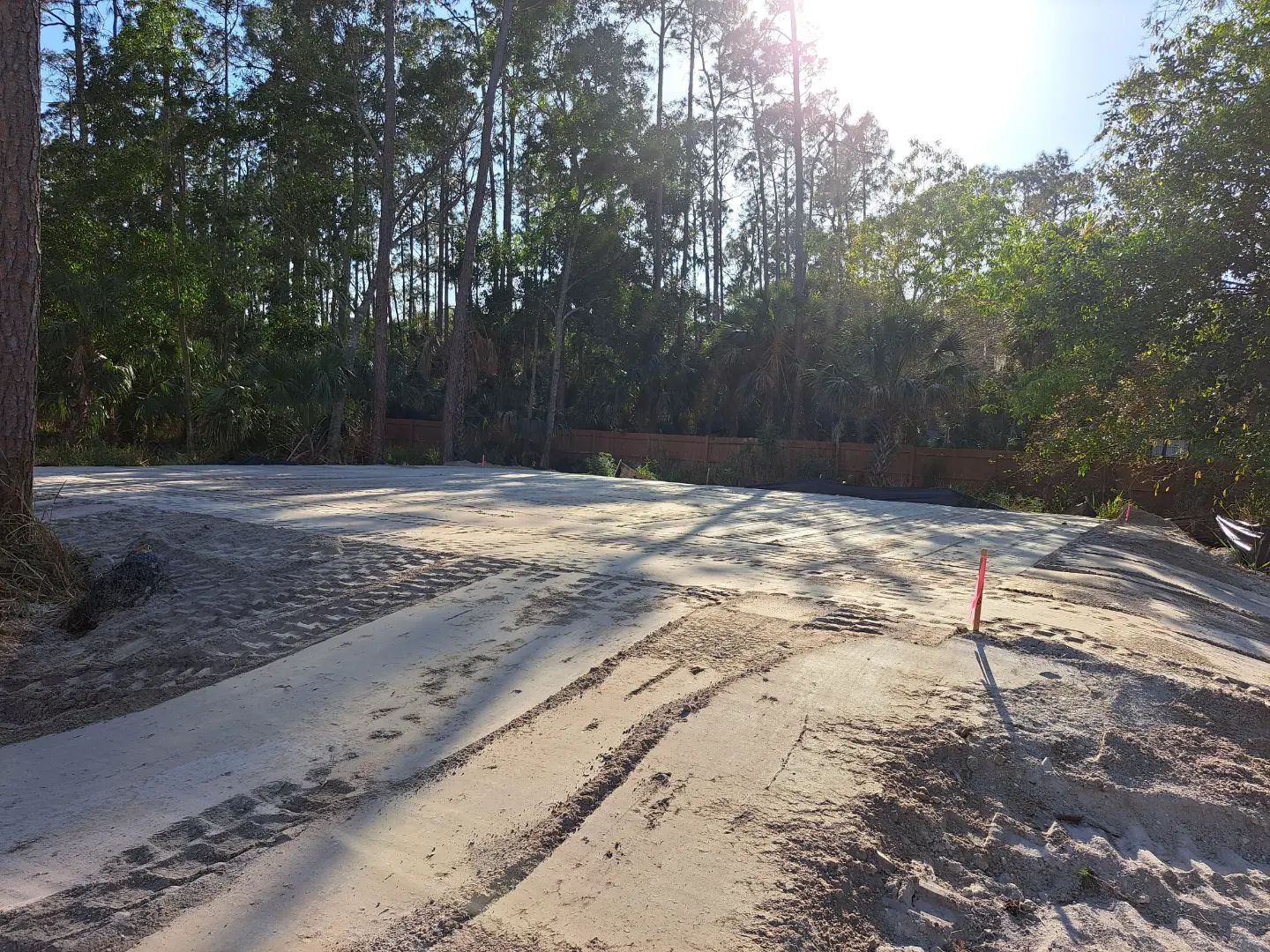 A dirt road with trees in the background and a red pole in the middle