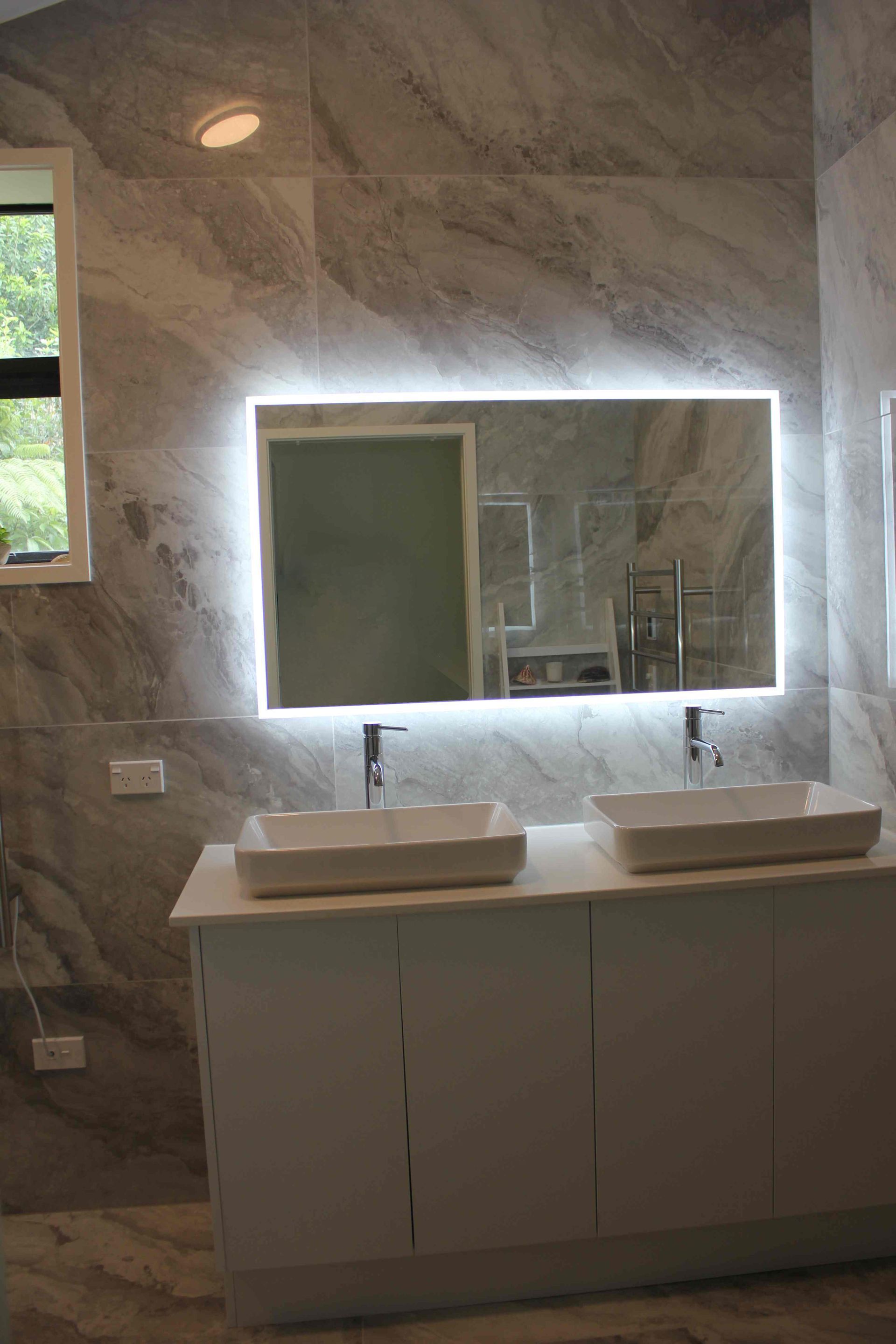 A bathroom with two sinks , a mirror and a window.