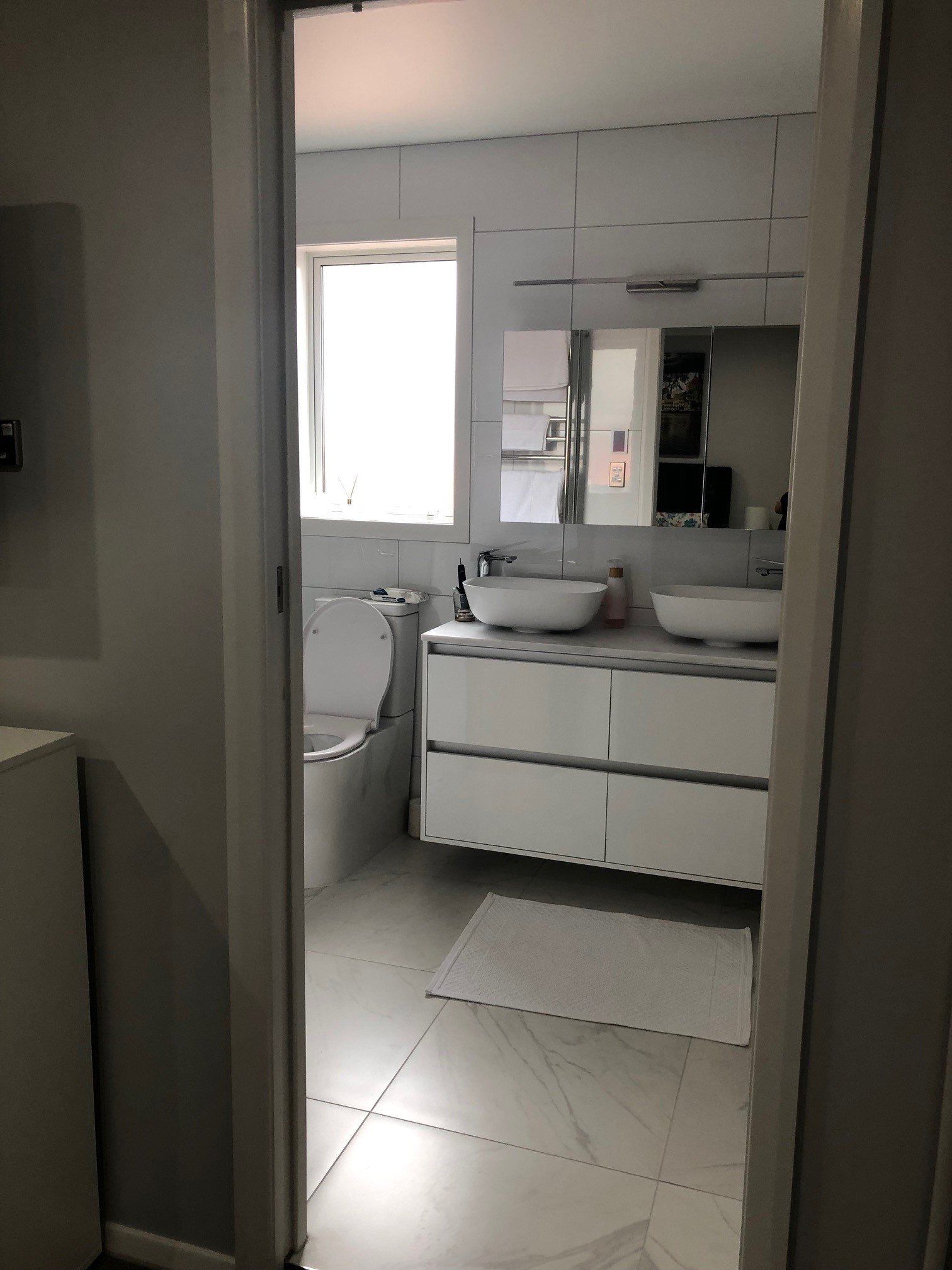 A bathroom with two sinks , a toilet and a window.