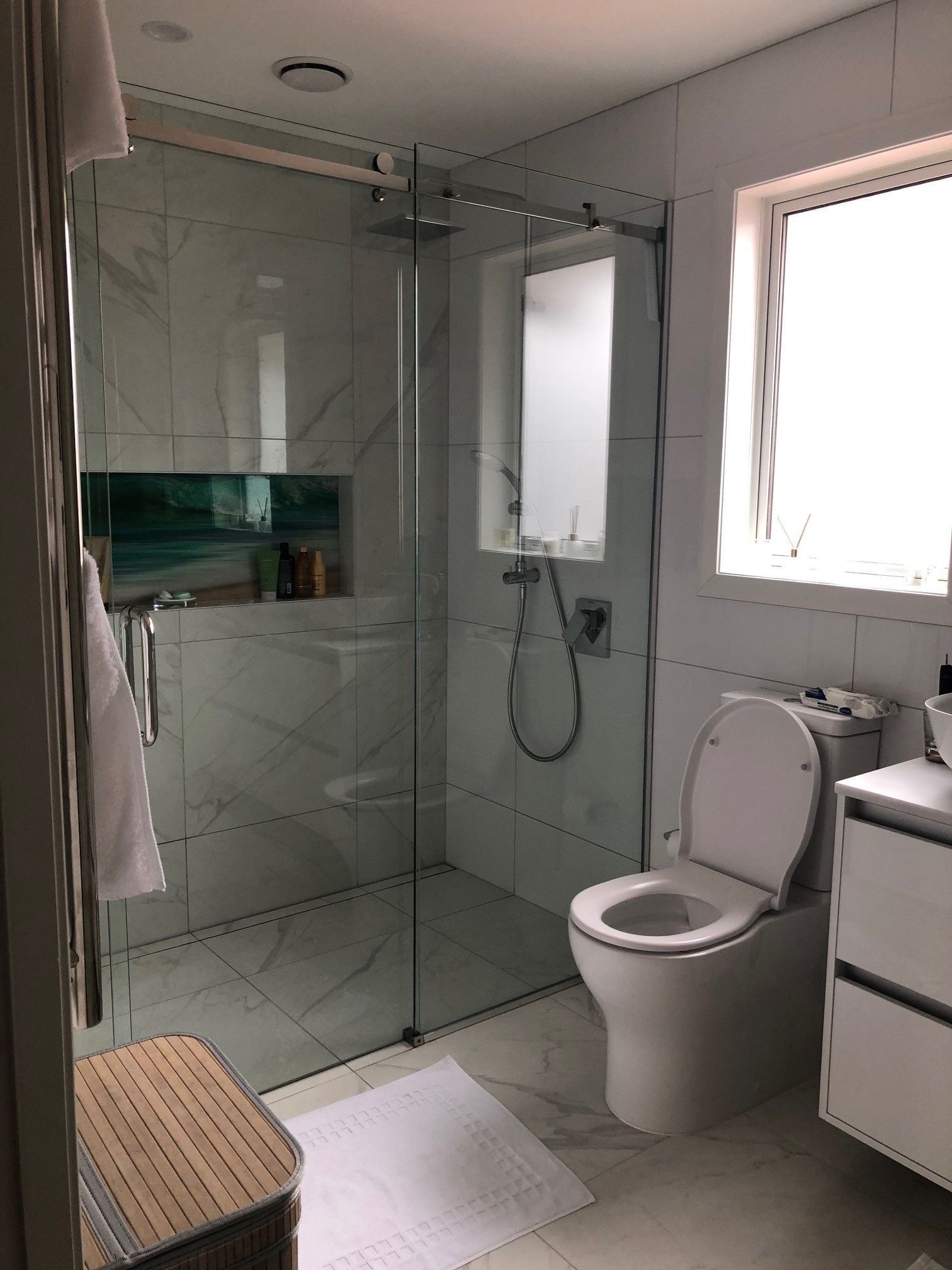 A bathroom with a toilet , sink , shower and window.