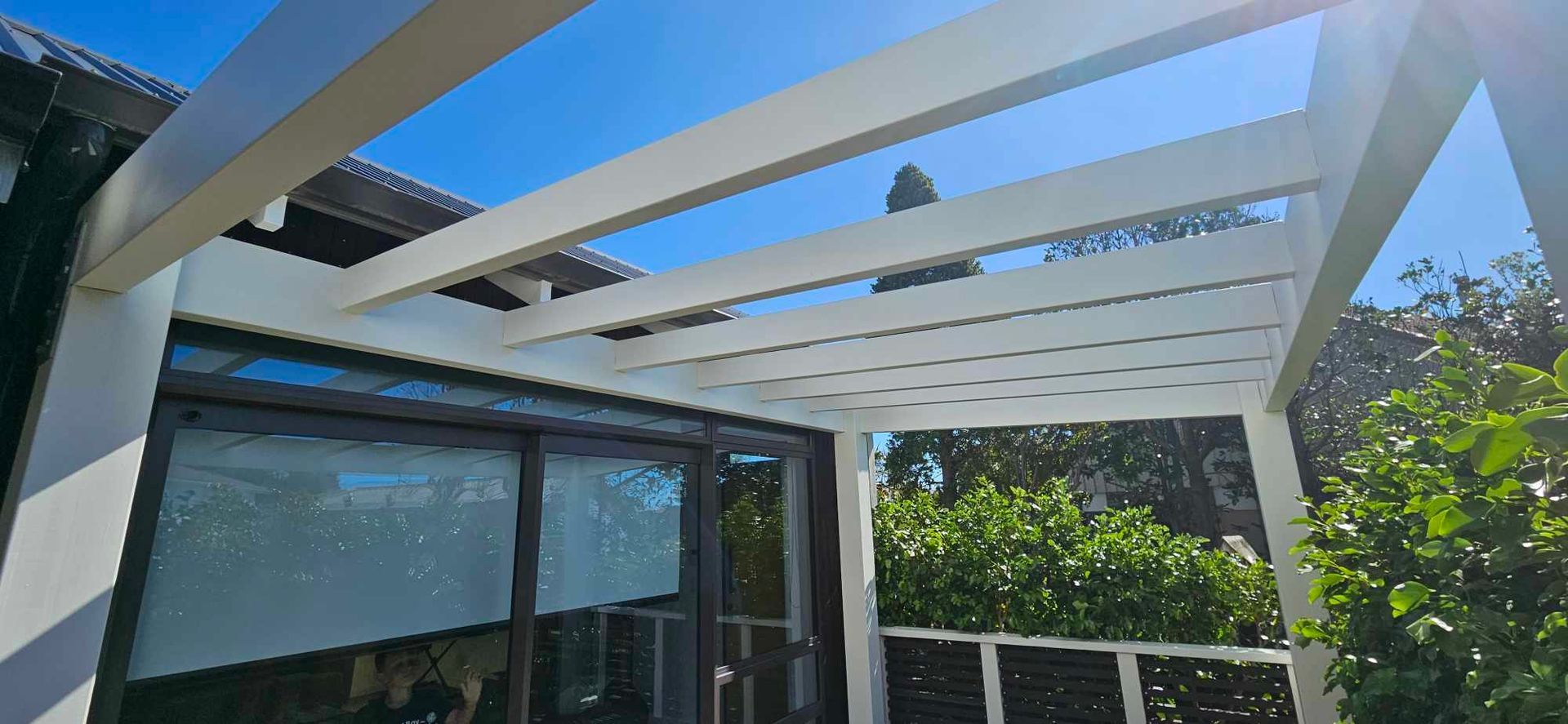 A white pergola is sitting on top of a patio next to a house.