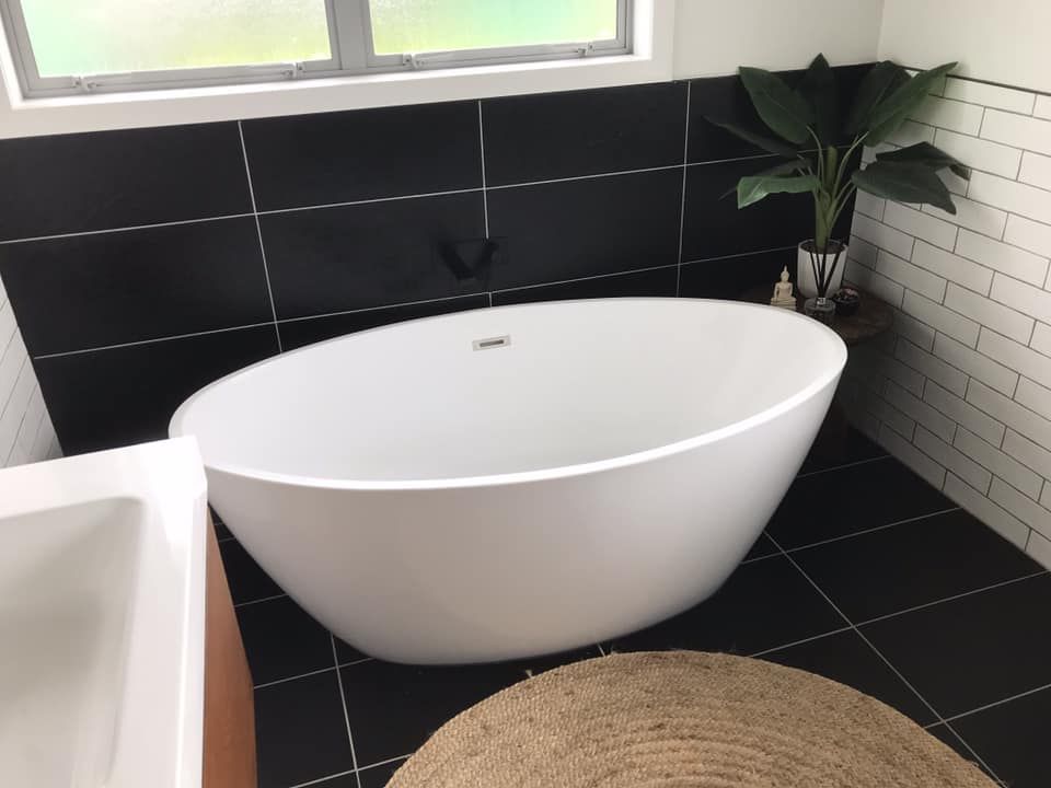 white ovla freestanding bath in black tiled bathroom with jute rug
