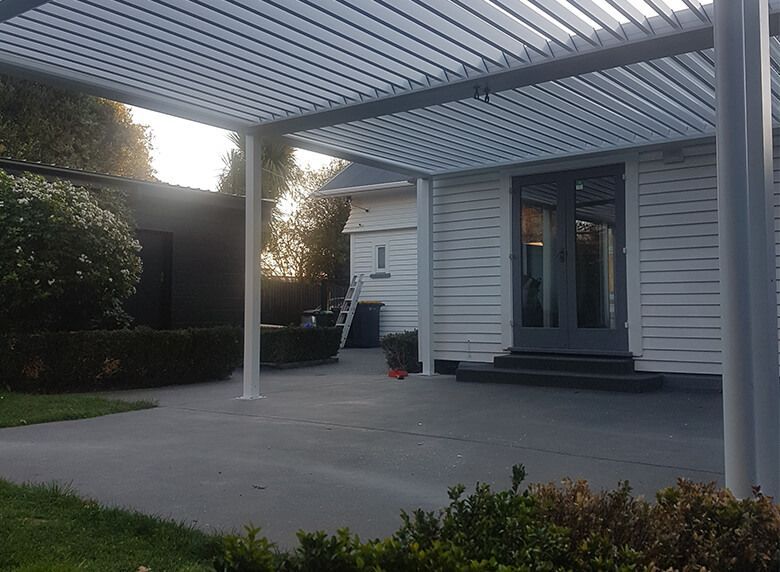 A white house with a patio and a pergola over it.