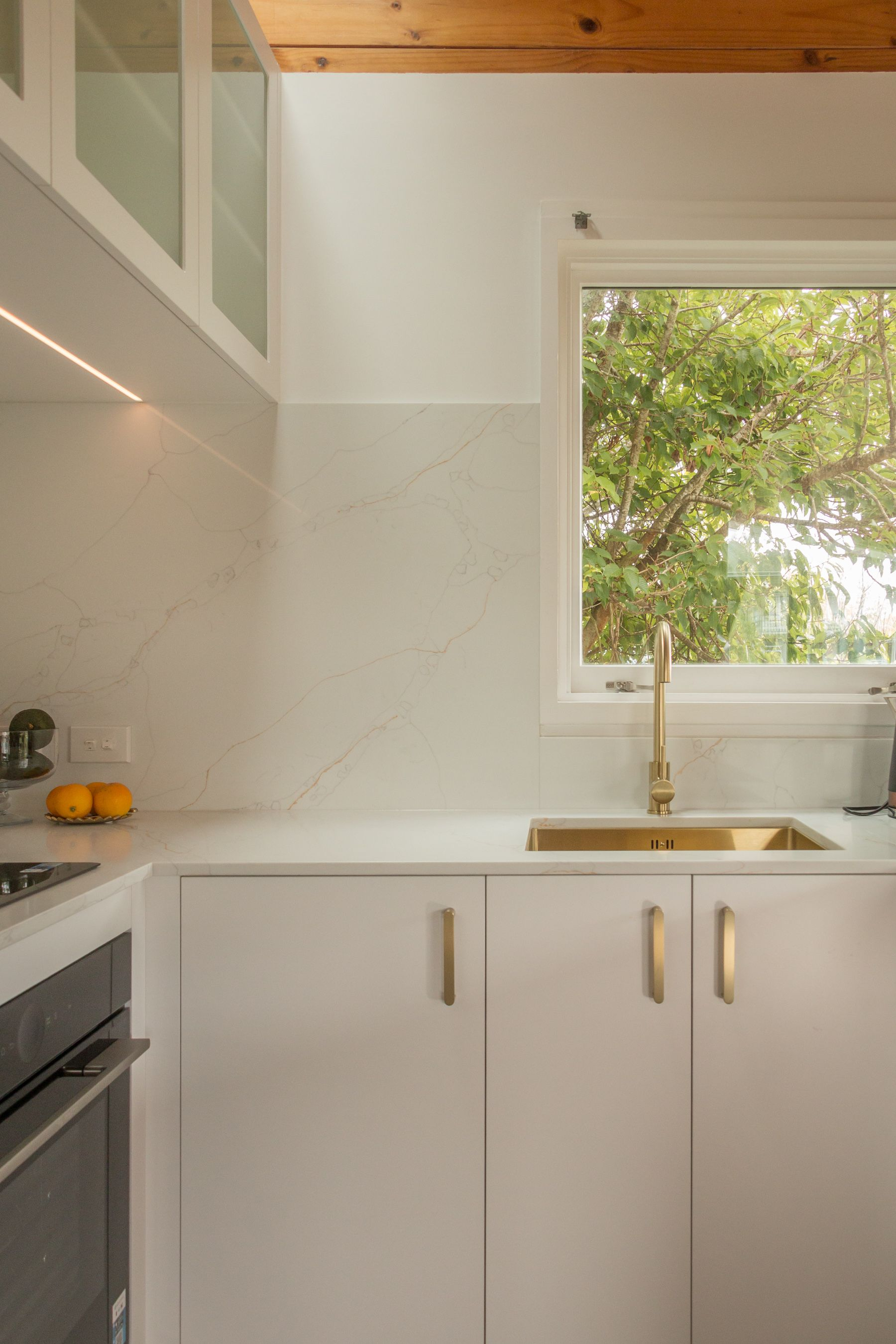 Modern white kitchen with wood ceiling, sink by a window, and white cabinets