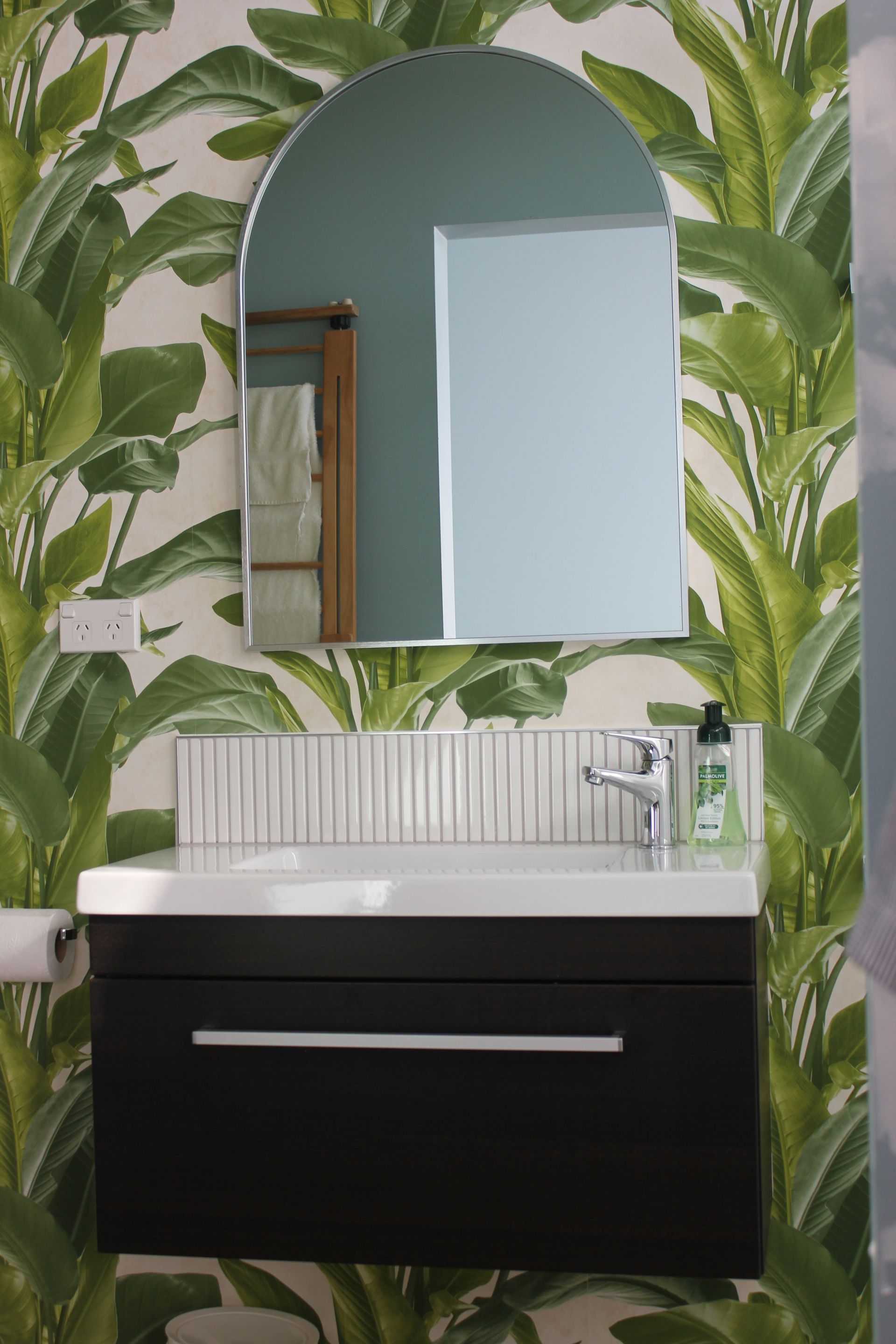 A bathroom with a sink , mirror and tropical wallpaper.