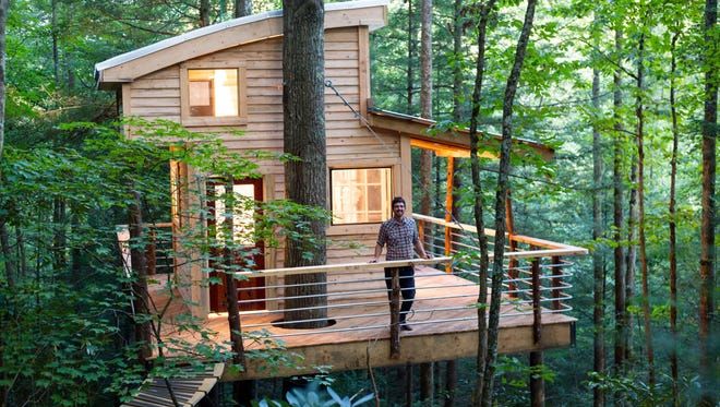 A man is standing on the deck of a tree house in the woods.