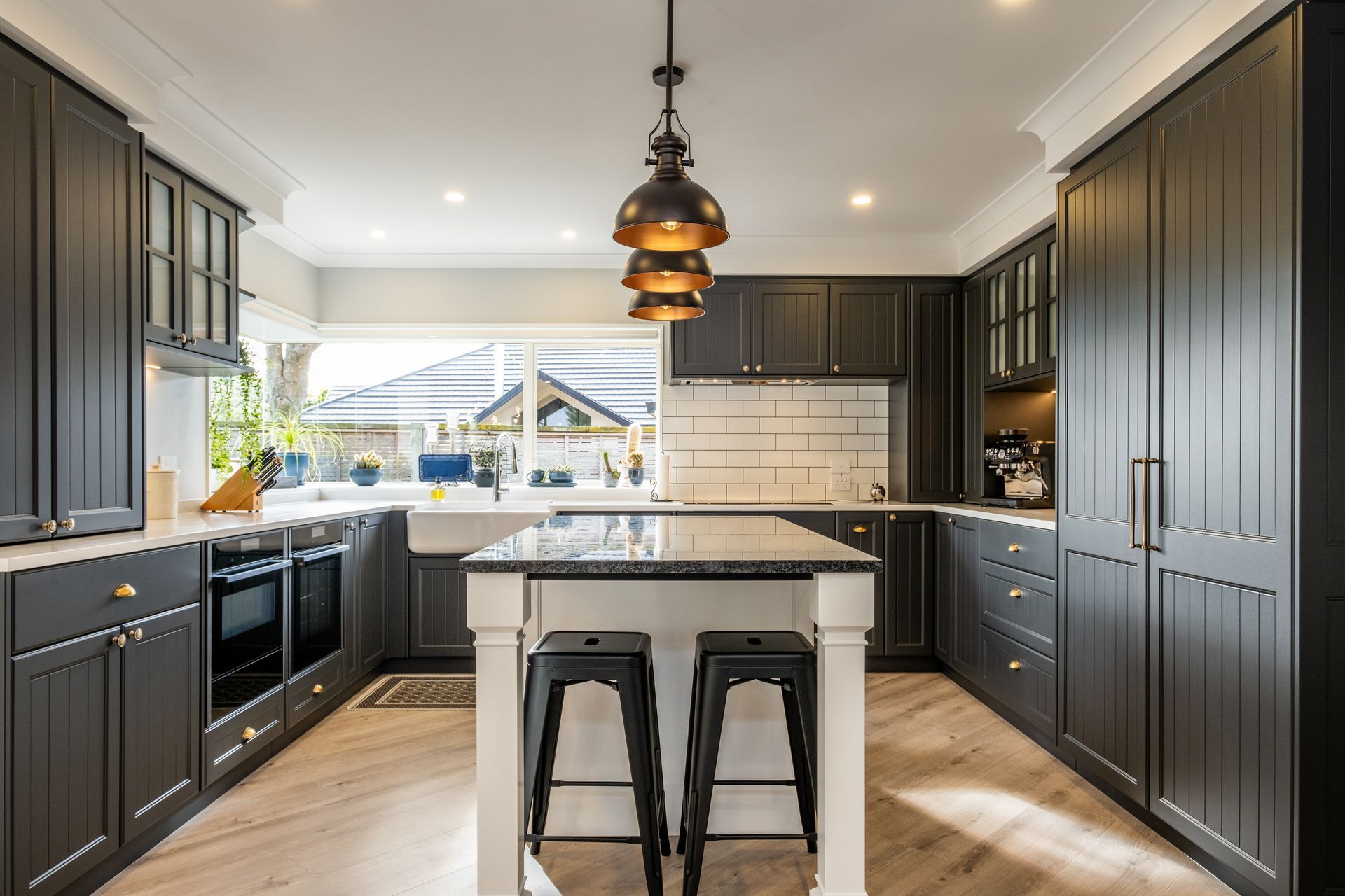 A kitchen with black cabinets and a white island with two stools.