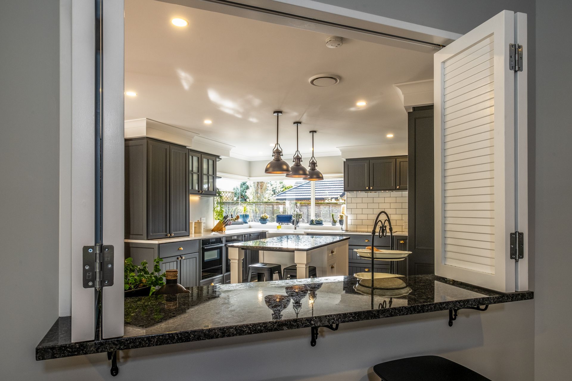 A view of a kitchen through a window with shutters open.