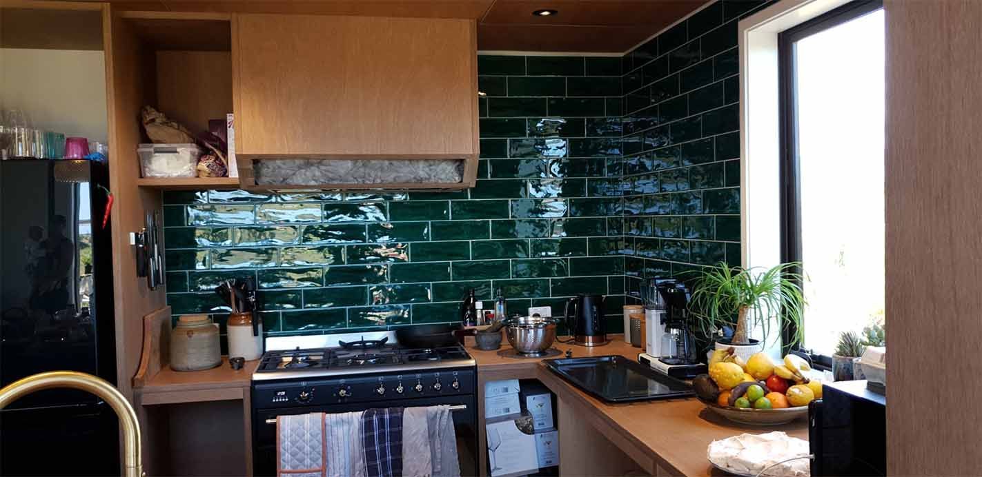 A kitchen with green tiles , a stove , a sink , and a window.