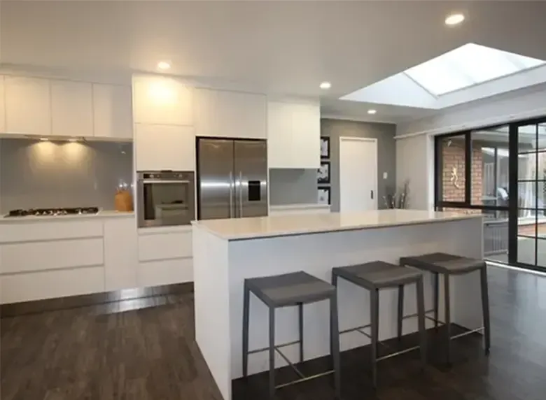 A kitchen with white cabinets and stools and a skylight