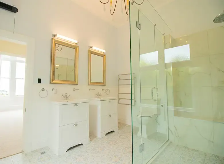 A bathroom with two sinks , a toilet , and a walk in shower.