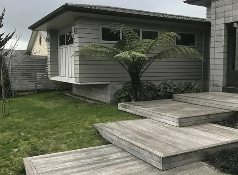 A house with stairs leading up to it and a tree in front of it.