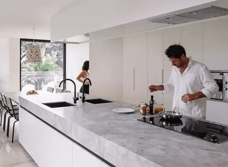 A man is cooking in a kitchen with a woman standing in the background.