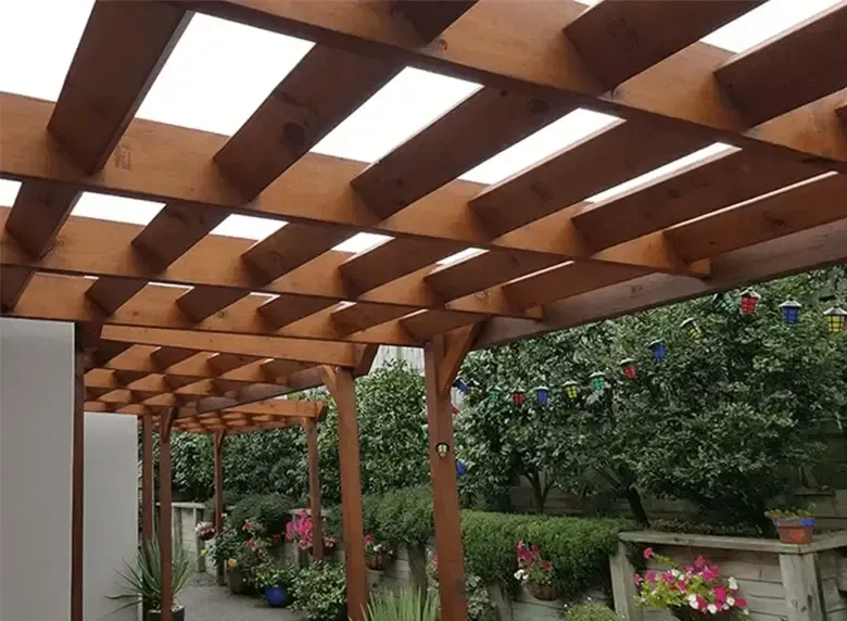 A wooden pergola with a clear roof is in a garden.