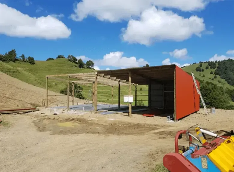 A red building is being built in the middle of a dirt field.