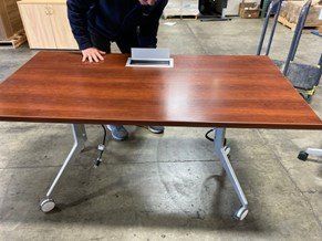 A man is standing next to a wooden table in a warehouse.