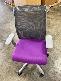 A purple office chair is sitting on a concrete floor in a warehouse.
