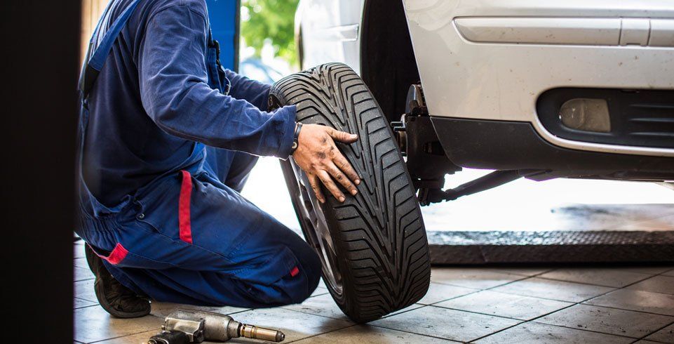 A Mechanic is Changing a Tyre on a Car in a Garage — Wheel Alignment Centre In Braitling, NT