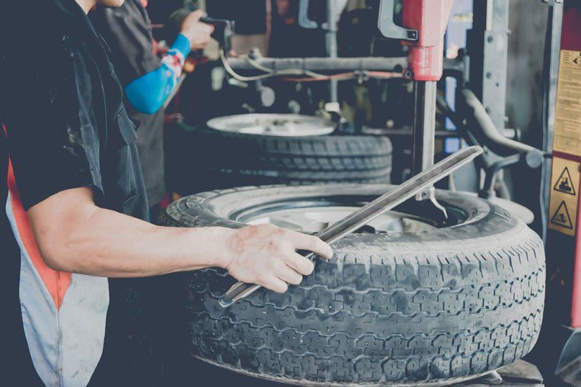A Man is Changing a Tyre on a Machine in a Garage — Wheel Alignment Centre In Braitling, NT
