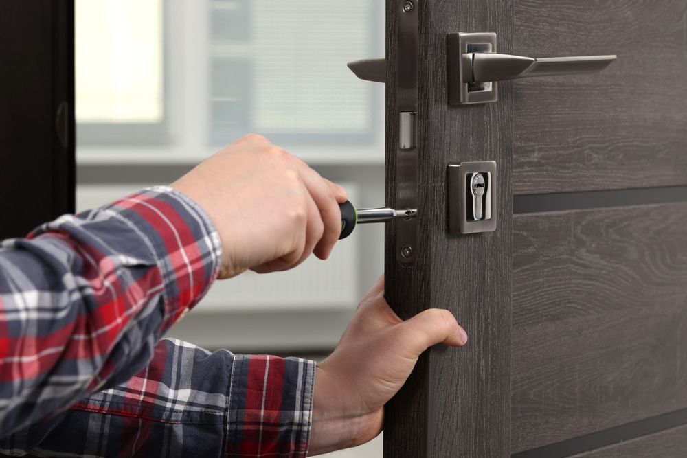 A Man Is Fixing A Wooden Door With A Screwdriver — New Lock & Safe Services in Port Campbell, VIC